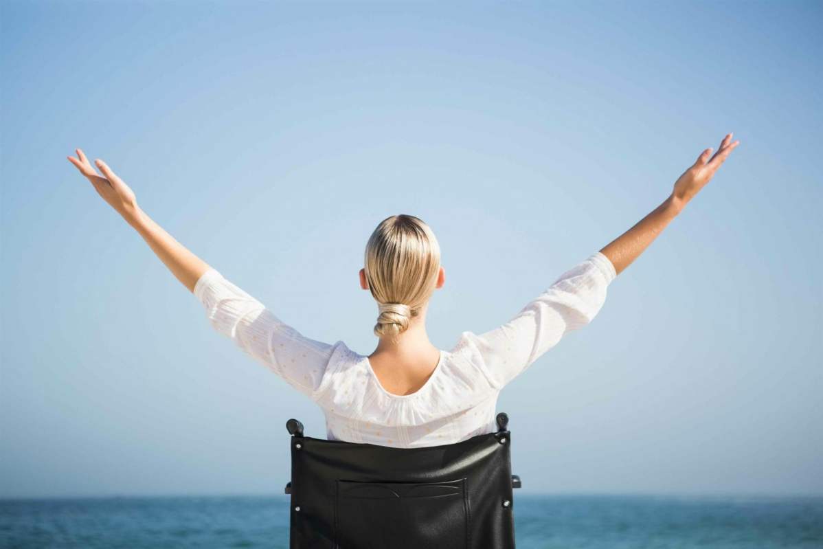 Rollstuhlfahrerin begrüßt das offene Meer indem sie beide Arme hochreißt
