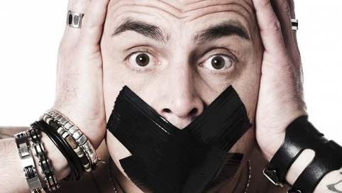Ein Mann hält seinen Kopf und guckt schokiert. Sein Mund ist mit einem X zugeklebt.