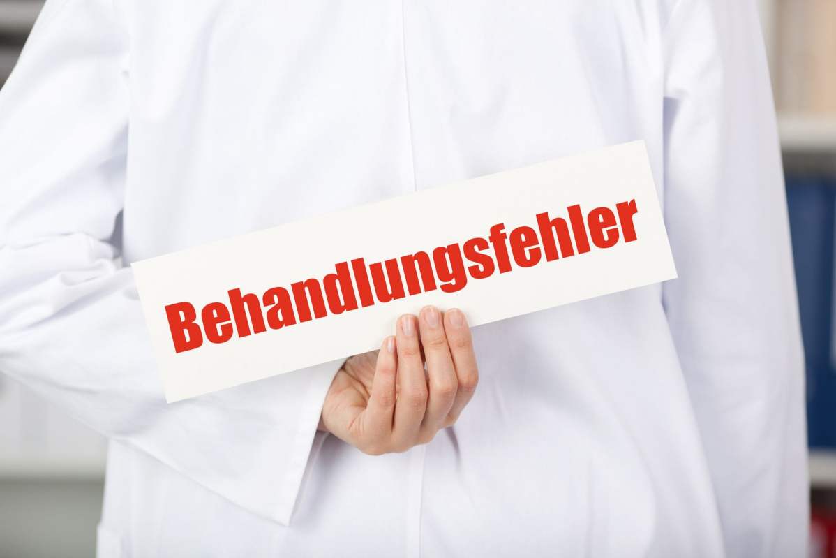 Ein Arzt hält hinter seinem Rücken ein Schild mit "Behandlungsfehler"