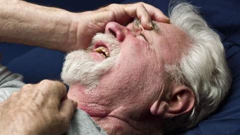 Foto: Ein Mann greift sich liegend und mit schmerzverzerrtem Gesicht an den leicht erhobenen Kopf.