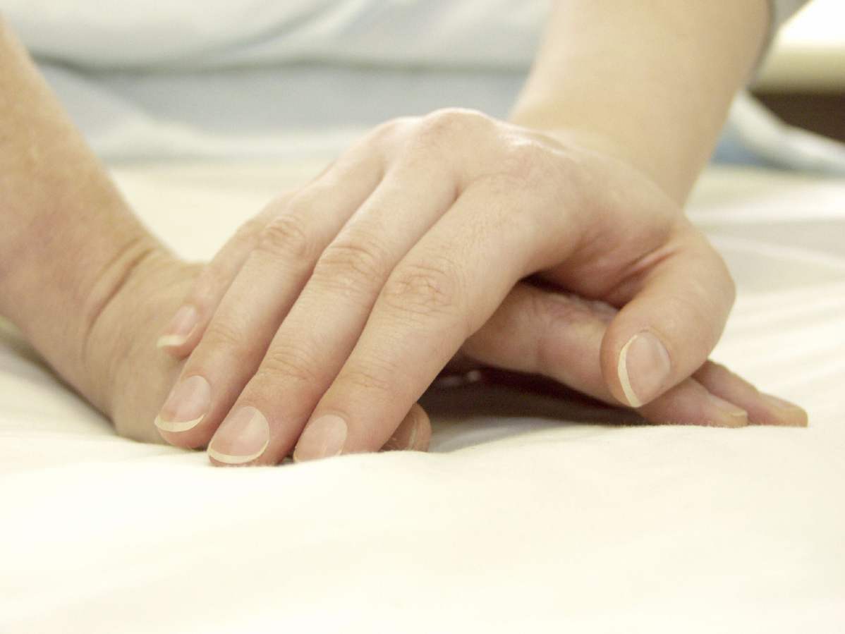 Eine Hand tröstet eine darunterliegende Hand eines anderen Menschen