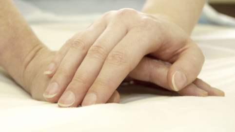 Eine Hand tröstet eine darunterliegende Hand eines anderen Menschen