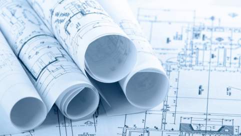 mehrere übereinander gestapelte Rollen von Bauzeichnungen auf einer ausgebreiteten Bauzeichnung