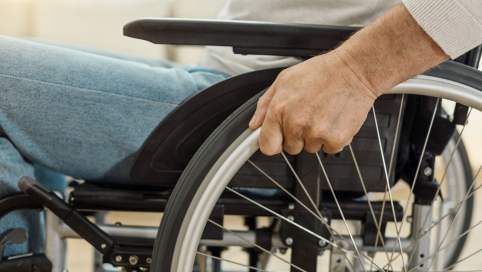 Foto: Ein Mann mittleren Alters sitzt in einem Rollstuhl. Der Bildausschnitt ist so gewählt, dass man keine Person erkennt