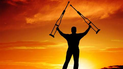 Ein Mann reist seine beiden Krücken vor einem Sonnenuntergang in die Höhe