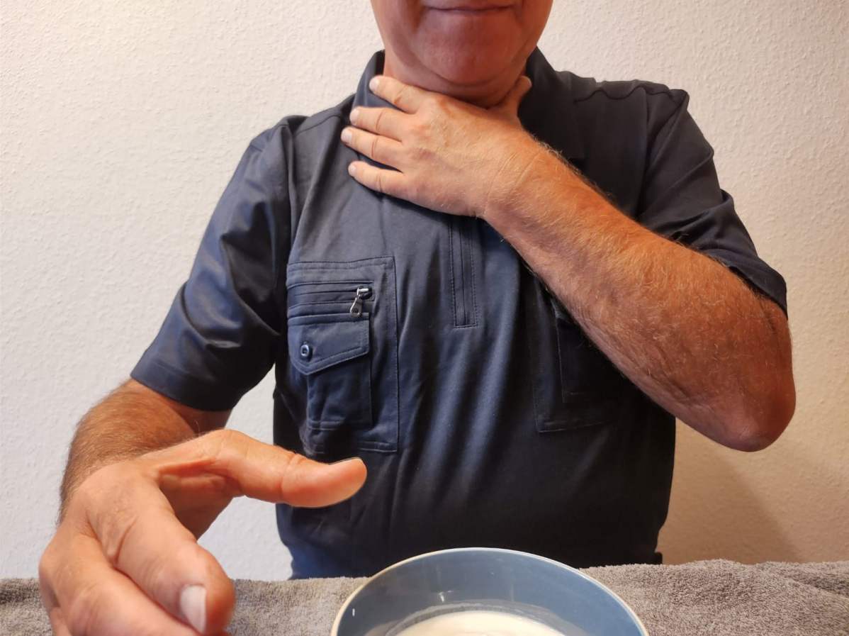 Ein Mann mit einer Schluckstörung fasst sich an den Hals vor einer Schale Essen